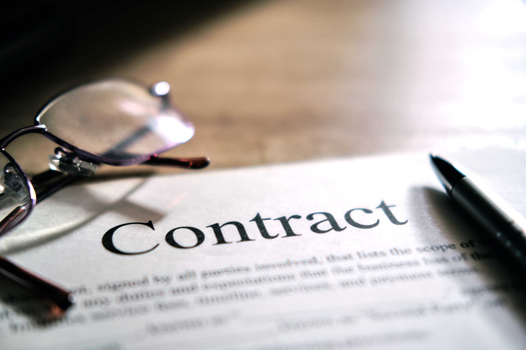 reading glasses and a contract and pen laying on a desk
